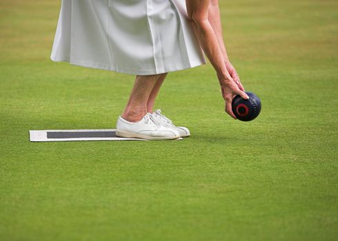 A mature lady player playing lawn bowls.