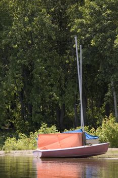 a small orange sail boat near the shore