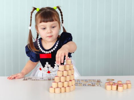 A little girl builds a tower of lotto sitting at the table