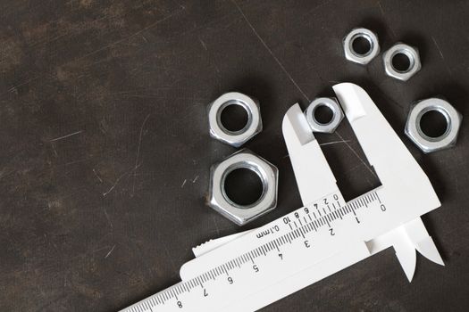 Few screw nuts and vernier callipers on dark metal background with copy space