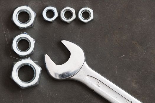 Closeup of spanner wrench and few screw nuts on dark metal background