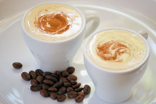 white cups with cappuccino with plums and cinnamon on a white dish