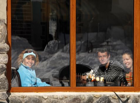 Three friends in cafe behind glass in which winter is reflected