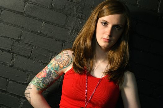 A young female with serious stare and arm tattoo.
