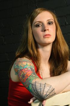 A young female with serious stare and arm tattoo.
