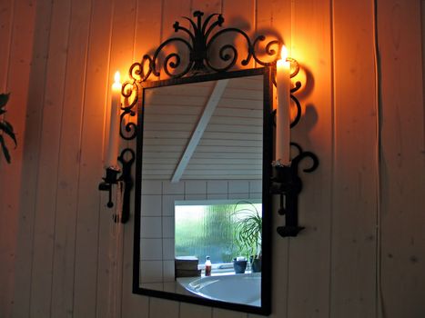 Decorative bathroom mirror with candle lights on a wood panels wall with reflection in the mirror