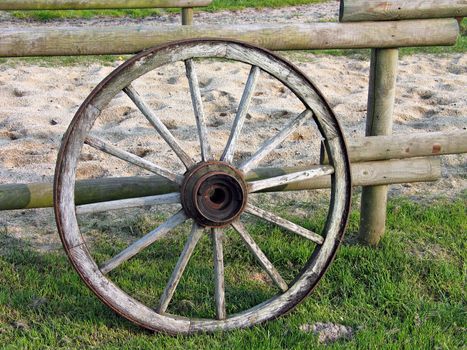 An old wooden wheel of a wagon leans on a ranch fence