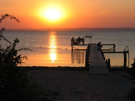 Family seats on a dock and enjoy the sun going down