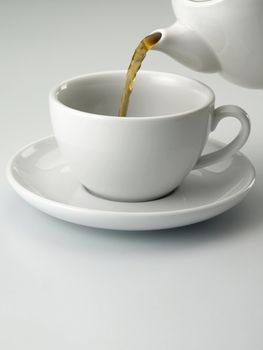 close up of a cup with tea and tea pot on the plain background