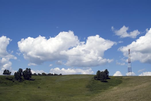 Telecommunication tower on the green field with blue sky.