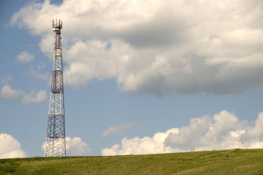 Telecommunication tower on the green field with blue sky.
