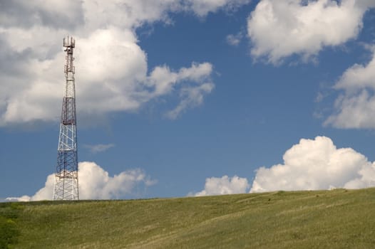 Telecommunication tower on the green field with blue sky.