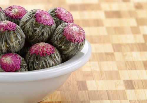 Several handsewn balls of flowering tea in a white bowl.