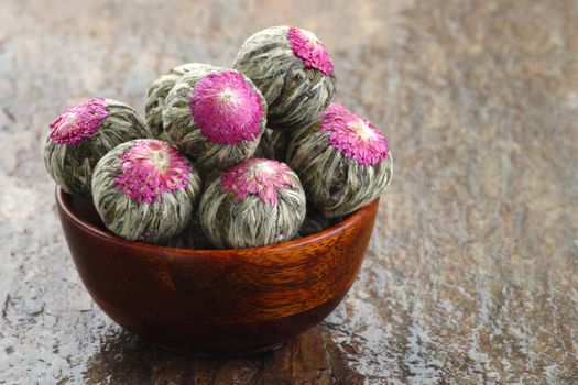 Several handsewn balls of flowering tea in a bamboo bowl.