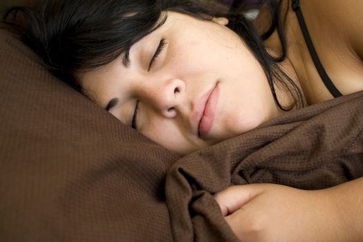 A young brunette woman is fast asleep in her bed.