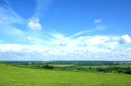 Summer landscape with a wide green valley and the blue sky with white clouds. 