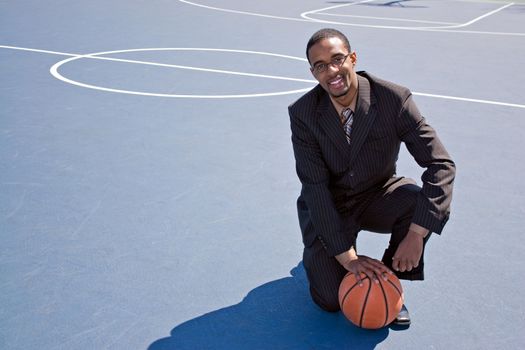 A young African American man in a business suit posing on the basketball court with a ball.  Works great for coaching or recruitment concepts.