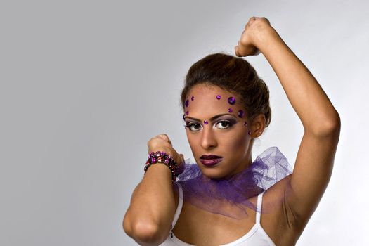 A young dancer with gemstones on her face isolated over a silver backdrop.
