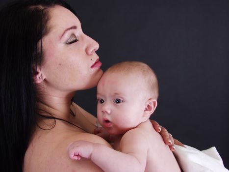 A mother with her eyes closed holding her child close. On a black background.