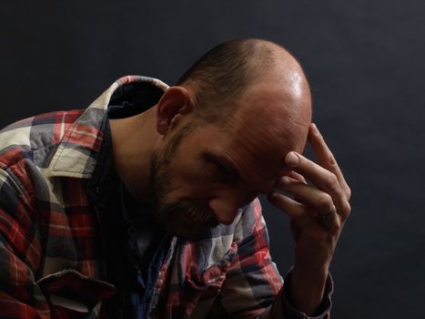 A man in deep thought holds his head in his hand. Over black.