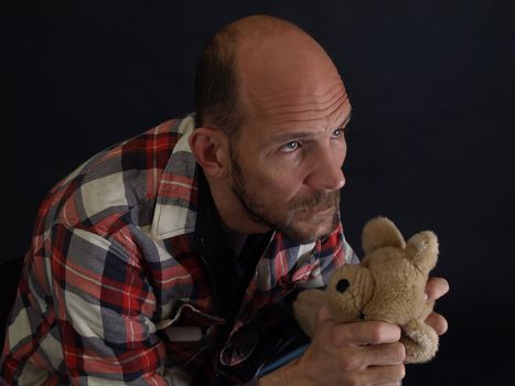 A man looking to the sky while holding a teddy bear isolated by a black back ground