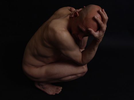 A bald nude male grips his head and neck. Over black.