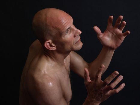 A shirtless male reaching upwards with both hands isolated on a black background