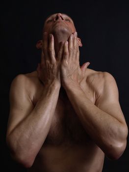 A shirtless man with his hands on his neck isolated by a black background