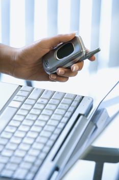 Close up of Asian/Indian young woman's hand holding cellphone with laptop in background.