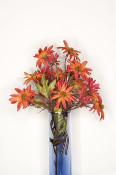 Still life shot of fake red flowers in blue vase.