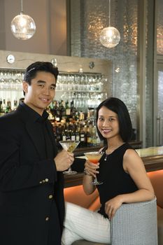 Prime adult Asian male and female at bar with cocktails.