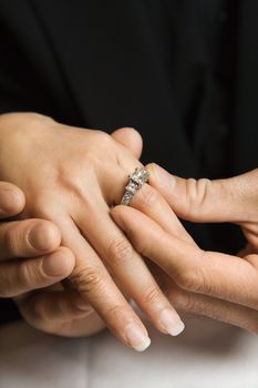 Prime adult Asian male putting engagement ring on female's hand.