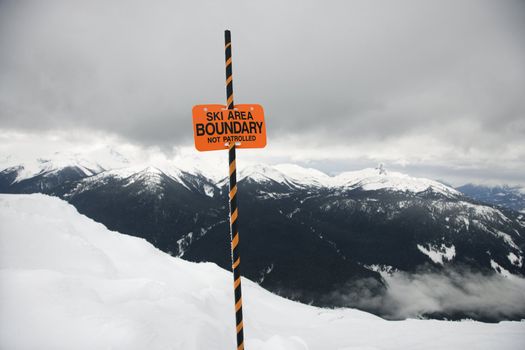 Ski area trail boundary sign with mountain landscape in background.