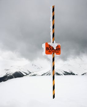 Ski area trail boundary sign in snow-covered mountain scene.