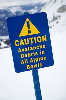 Snow ski resort caution sign on mountain side.