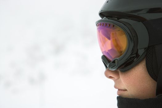 Profile of Caucasian teenage boy skier wearing helmet and goggles at ski resort on mountain.