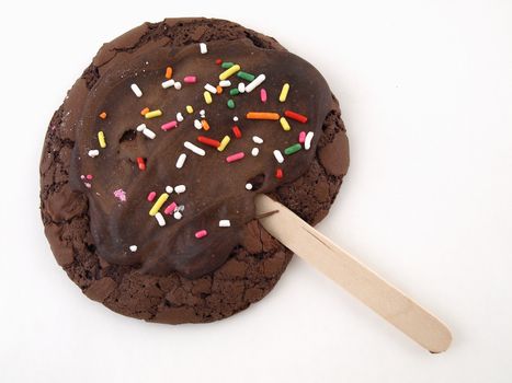 A chocolate cookie with sprinkles and frosting on a stick isolated on a white background