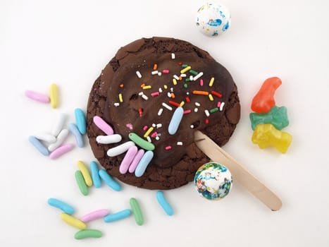 A chocolate frosted cookie with sprinkes, and other colorful candies isolated on a white back ground