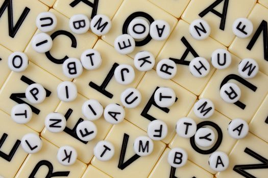 white beads with black letters spilled randomly on an ivory mosaic with bigger letters