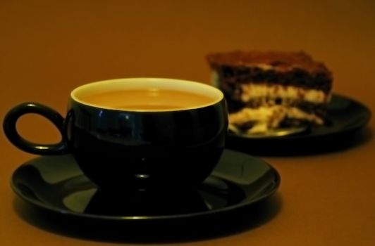 Stylish black cup of white coffe with black forest gateu in the background.