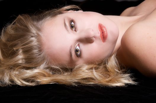 Beautiful young blond woman lying on black background