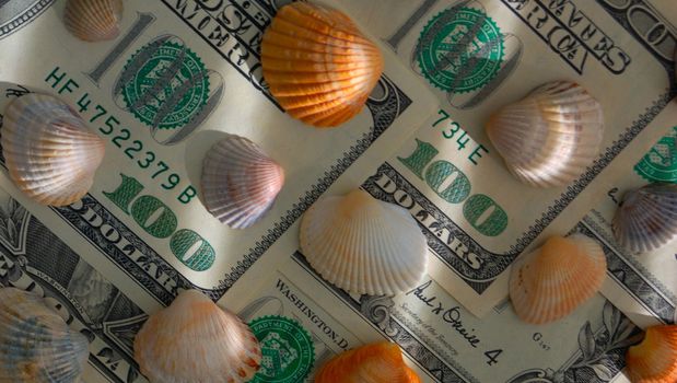 How mach is the summer travel? Close-up of 100 dollar bill and shells of different colors