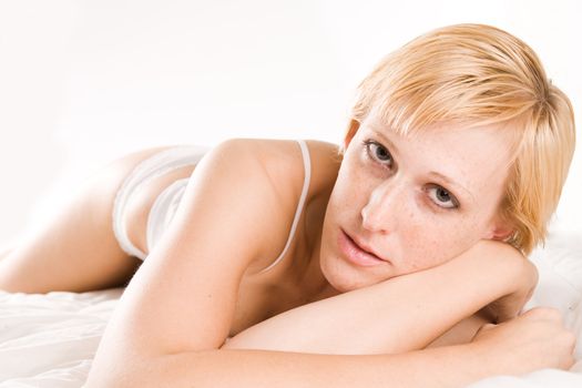 Studio portrait of a blond short haired girl in lingerie laying on her bed flirting with you