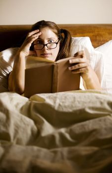 Woman reading in bed with a shocked expression