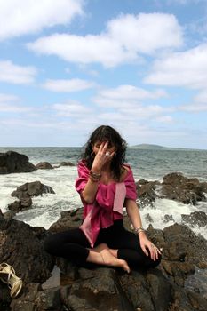 beautiful woman meditating on the rocks in ireland with her eyes closed, in the lotus position, showing a healthy way to live a happy and relaxed lifestyle in a world full of stress