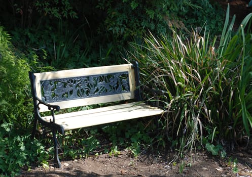 A wooden and iron bench sits in a lush garden