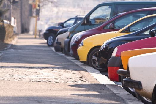 Row of different cars parked in a crowded city.