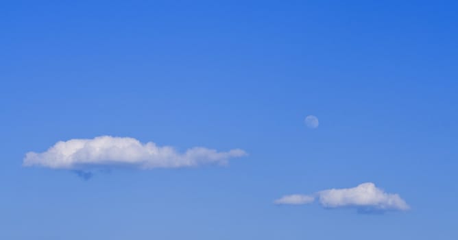 Clouds and moon on a blue sky in a late afternoon.