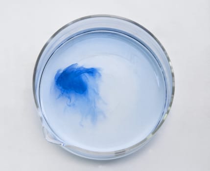 Blue substance dissolving in a glass recipient-upper view.