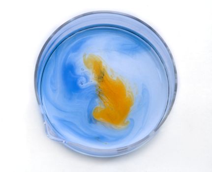 Blue and orange substances dissolving and blending in a glass recipient-upper view.